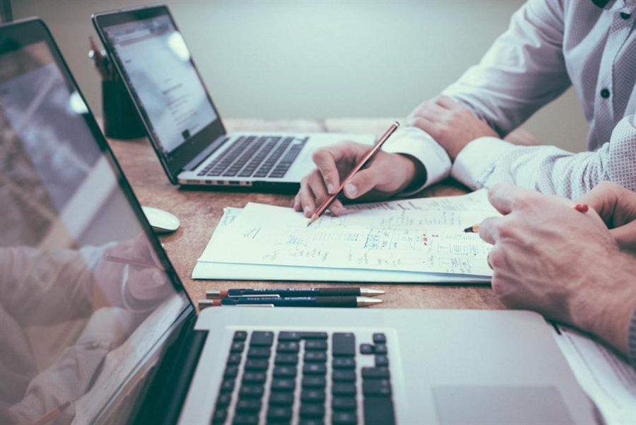 Manos revisando documentos empresariales junto a un computador portátil